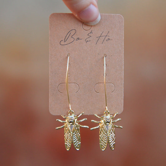gold cicada earrings dangling below long gold ear wires